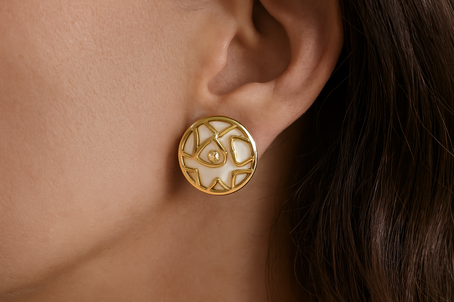 Elegant gold geometric earrings with white enamel and crystal centers being worn